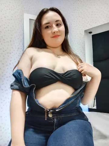 Curvy woman in a black bandeau top and denim jeans sitting in a bright room.