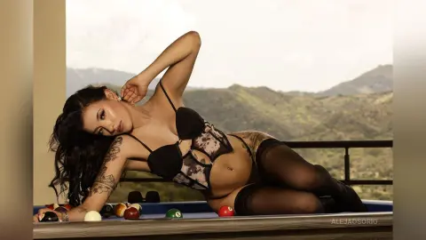 Aleja reclines on a blue pool table wearing black lace lingerie and sheer black stockings.