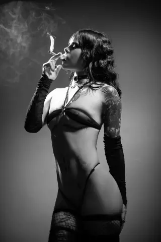 Moody black and white portrait of a woman in black lingerie and lace gloves smoking a cigarette.
