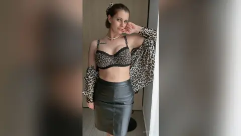 Woman in leopard print bra and black leather skirt posing in a modern indoor setting.
