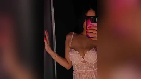 Young woman in a pink lace lingerie bodysuit posing in a dimly lit bedroom for a moody aesthetic selfie.