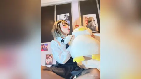 Young woman in a white shirt and black skirt hugging a large white penguin plushie in a cozy bedroom setting.