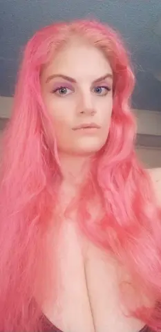 Portrait of a woman with long wavy pink hair and purple eyeshadow in a soft, dreamy indoor setting.