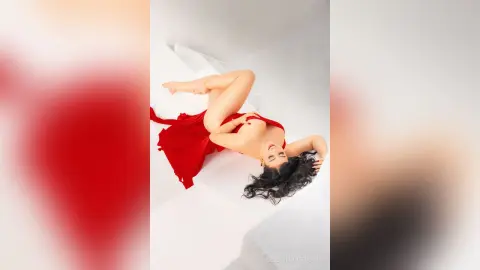 Glamorous woman in a flowing red dress lounging on a white surface with a dreamy, elegant mood.