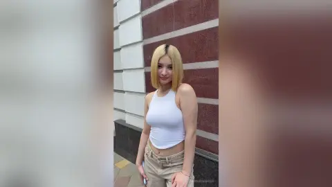 Blonde woman in a white tank top and khaki pants posing against a red and white striped wall.