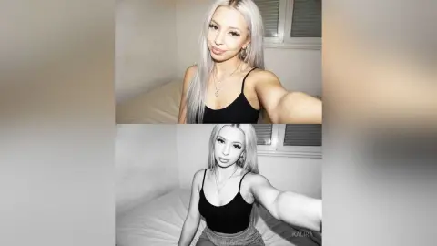 Kalira poses in a black tank top and silver necklace, showing off her long blonde hair in a bedroom setting.