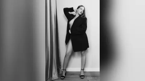 Elegant woman in a black oversized blazer posing in a minimalist studio setting, black and white moody portrait.