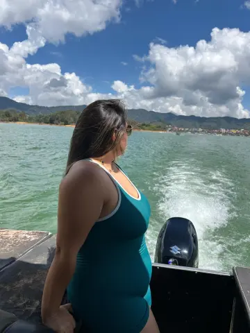 Woman in a teal swimsuit relaxing on a boat on a sunny day overlooking turquoise ocean waves and mountains.