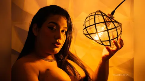 Moody portrait of a woman with dark hair wearing a silver necklace by warm glowing lantern light.