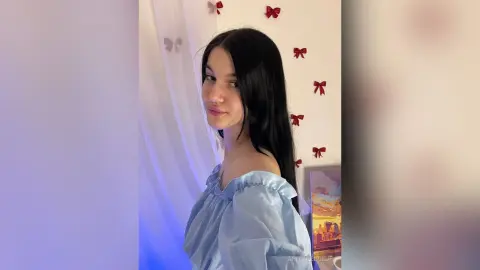 Young woman in a light blue off-the-shoulder blouse posing in a room decorated with red bows.