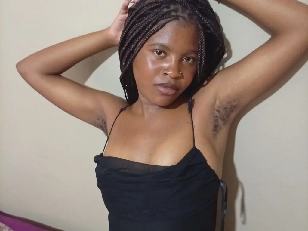 Young woman with braided hair in a black camisole posing confidently against a neutral wall.