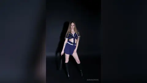 Fashionable young woman in a navy blue crop top and mini skirt posing against a dark studio background.