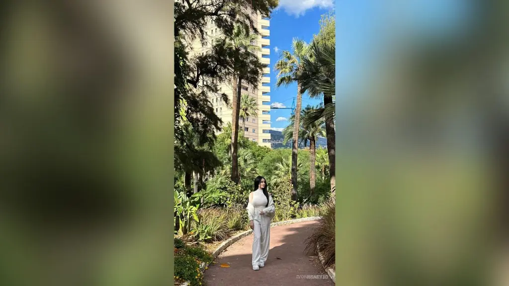 HoneyJo — HoneyJo stands on a paved path in a white long-sleeve top and white pants, surrounded by tropical palm trees and greenery.