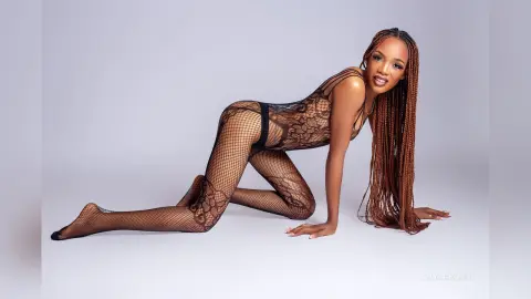 Beautiful woman with long braids wearing a black lace bodysuit posing on a white studio background.
