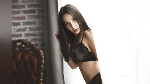 HelenaMacey poses in black lace lingerie, leaning against a wall with her long brown hair falling over her shoulder.