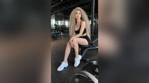 Athletic woman in black gym outfit sitting on a weight bench in a modern fitness center.