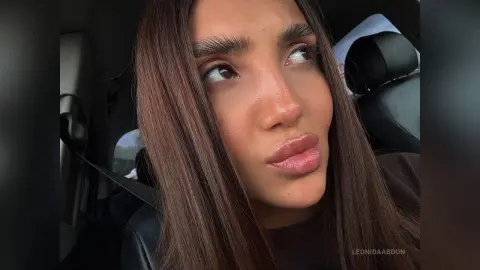 LeonidaAbdon looks up with long brown hair and full lips while sitting in a car seat.