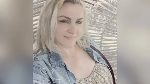 CandanceSmith smiling in a denim jacket and floral top while sitting outdoors.