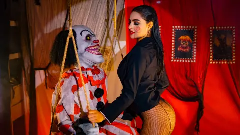 Woman in black outfit posing with a creepy clown puppet in a spooky red room setting.