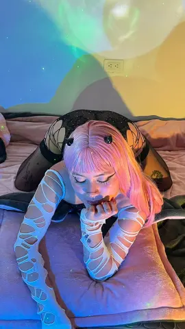 Vakker_Meilee, wearing black mesh or lace lingerie and white cut-out sleeves, poses on a pink bed with pink hair and blunt bangs.