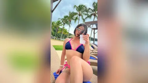 Young woman in a pink bikini relaxing on a lounge chair at a tropical beach resort.