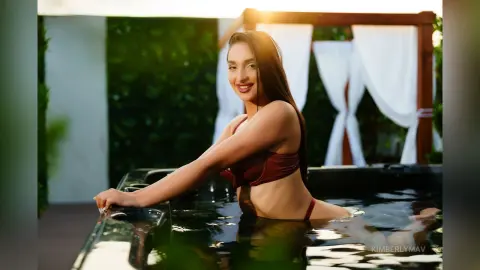 Smiling woman in a burgundy bikini relaxing in a luxury outdoor hot tub at a sunny tropical resort.