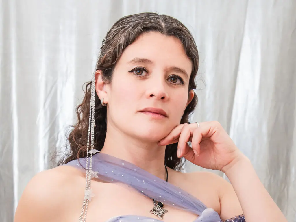Serene woman in a lavender tulle dress with silver hair accessories posing against a white curtain backdrop.