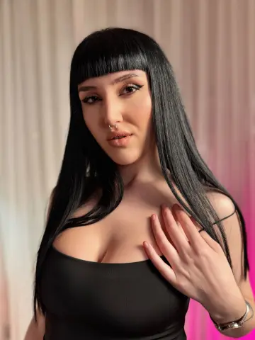 WendyyLuv poses with long black hair and blunt bangs, wearing a black tank top while resting her hand on her chest.