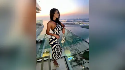 Elegant woman in a black and white zebra print dress posing on a luxury balcony at sunset overlooking the ocean.