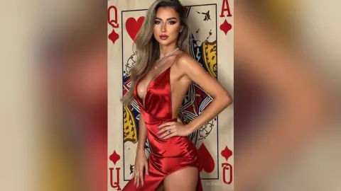 Glamorous woman in a red satin evening gown posing against a giant Queen of Hearts playing card background.