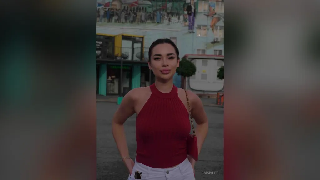 EmmyLee — EmmyLee stands outdoors in a red halter top and white pants with her hands on her hips.