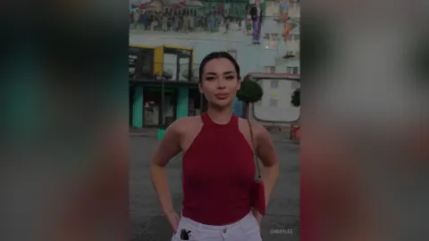 EmmyLee — EmmyLee stands outdoors in a red halter top and white pants with her hands on her hips.
