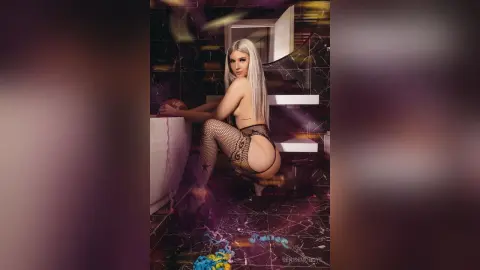 Blonde woman in black fishnet lingerie posing in a moody, dark marble bathroom setting.