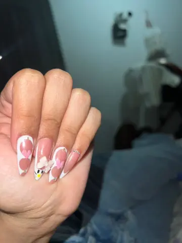 Close-up of long almond-shaped manicured nails with white French tips and pink heart nail art designs.