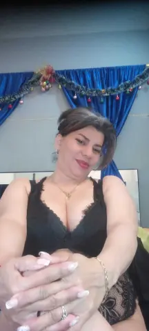 Smiling woman in a black lace camisole relaxing in a room with blue curtains and festive decorations.