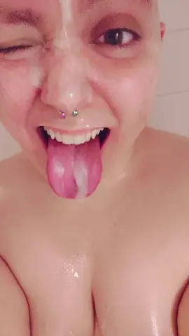 Close-up of a playful woman with a nose piercing sticking her tongue out in a wet, intimate setting.