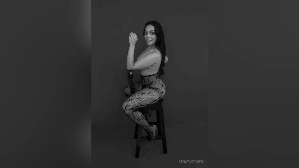 RenataBrown — Smiling woman in patterned leggings sitting on a stool in a moody black and white studio portrait.