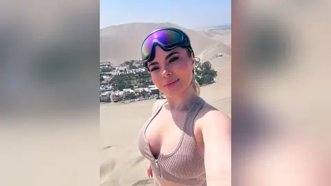Smiling woman in a ribbed beige bikini top and sunglasses posing in a vast desert landscape.