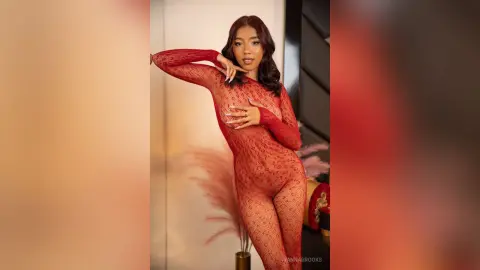 Beautiful woman in a red lace bodysuit posing elegantly in a warm, modern indoor setting.