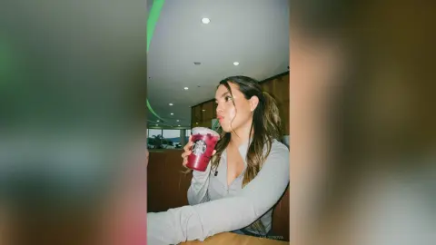 Young woman in a grey long-sleeve shirt sipping a drink in a modern cafe setting.
