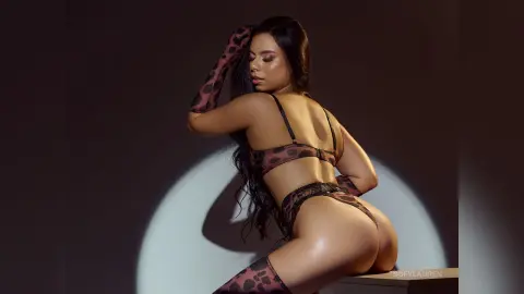 SofyLauren poses in a spotted bra and matching lace panties, showing her bare back and buttocks against a dark background.