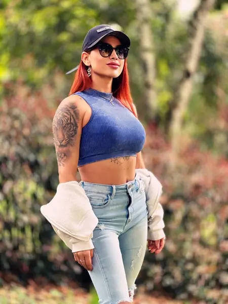 KataMajana poses with a slight pout, showing her long red hair and black tank top against a soft, natural outdoor background.