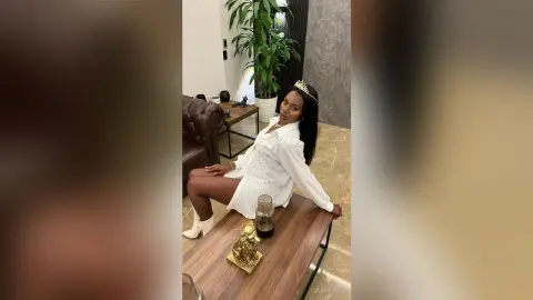 Elegant woman in a white shirt and crown sitting in a modern living room with a sophisticated mood.