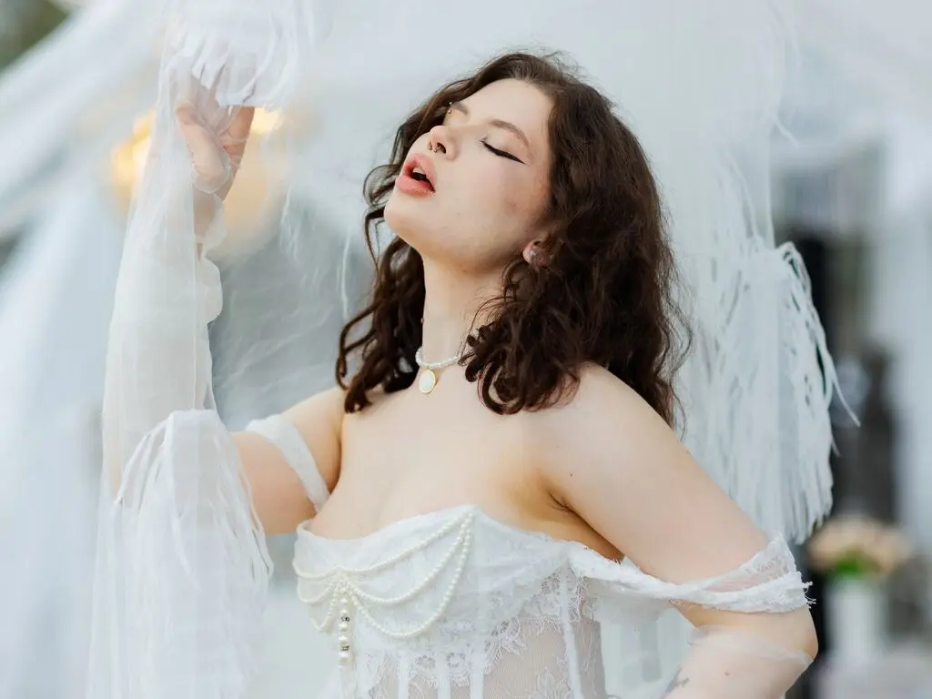 Dreamy portrait of a woman in a white lace bridal gown and pearl necklace posing under a sheer veil.