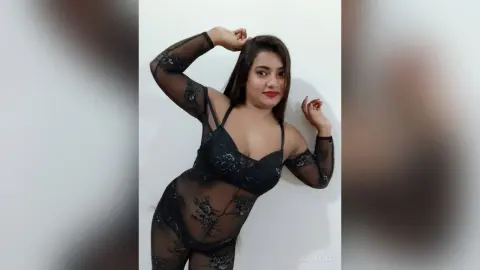 Young woman in a black lace bodysuit posing confidently against a white background.