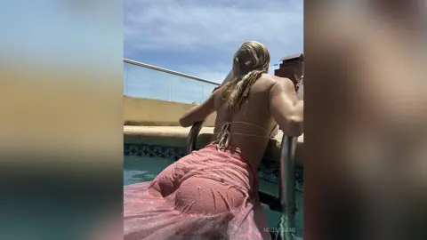 MielVerane shows her bare back and blonde hair while wearing a sheer pink wrap, sitting on the edge of a pool.