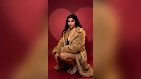 Elegant woman in a luxurious tan faux fur coat posing against a romantic red background.