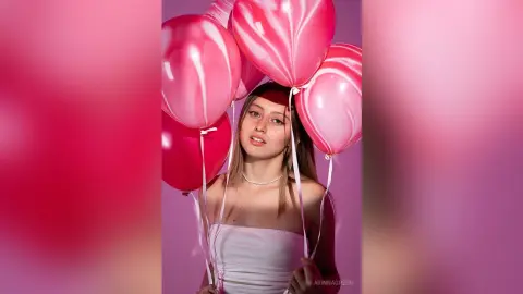ArinnaGreen poses with pink and white marbled balloons, wearing a white strapless top and a pearl choker against a pink background.