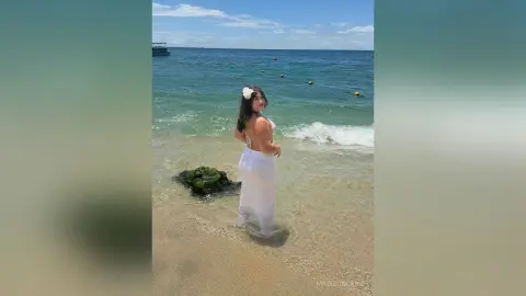Young woman in a white summer dress standing on a sunny tropical beach by the ocean waves.