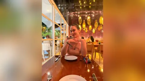 Young woman in a pink top sitting at a restaurant table under warm golden lighting.